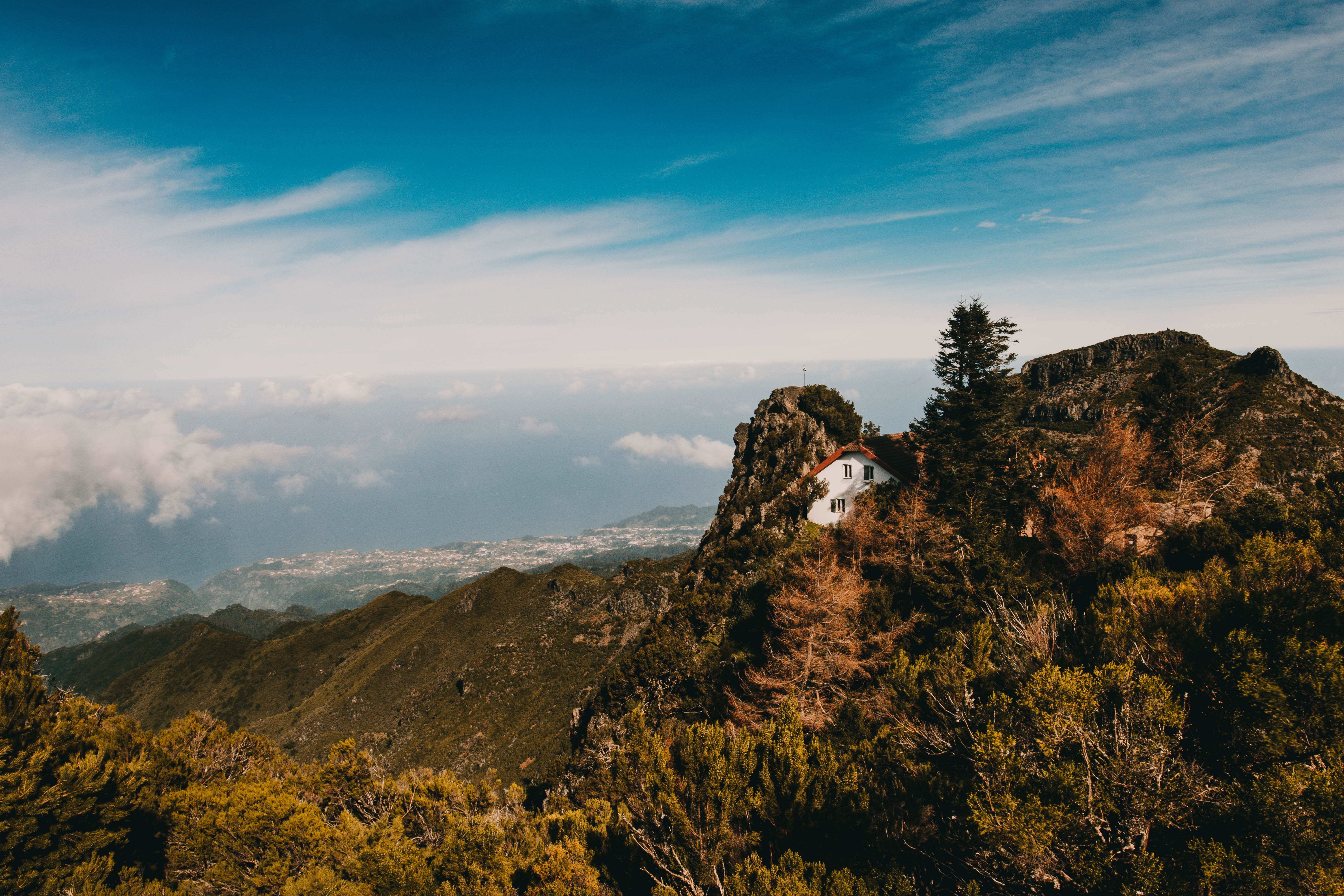 Small white house perched on rocky cliff above a sea of clouds