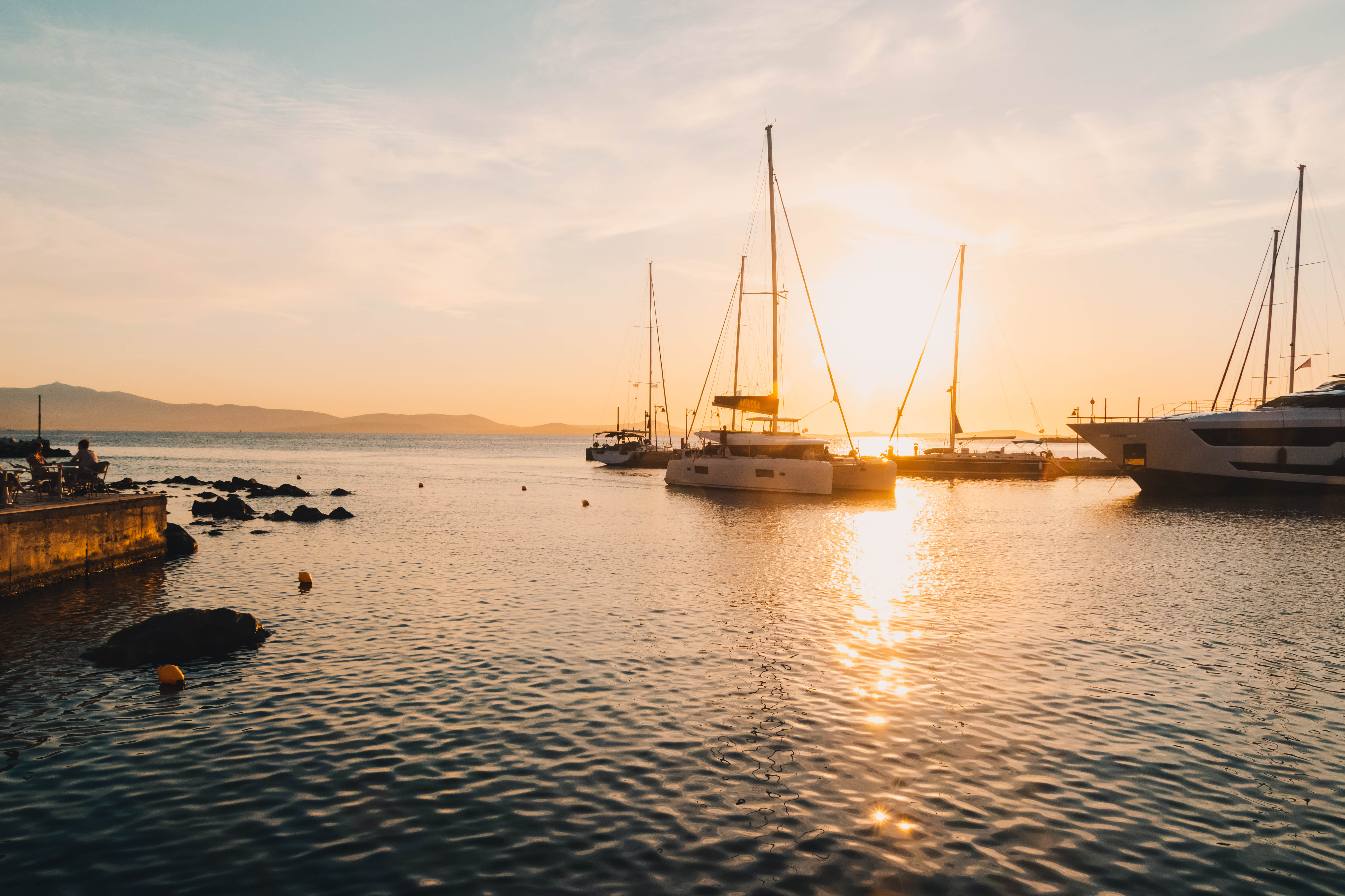 Sailboats silhouetted against golden sunset light on still harbor water, Funchal Marina